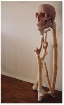 A standing assemblage of pale bones and branch-like limbs supporting a pink skull, photographed on a parquet floor.