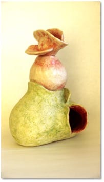 A green and pink glazed vessel topped with a flared trumpet-like opening, a dark hollow cut into its lower side.