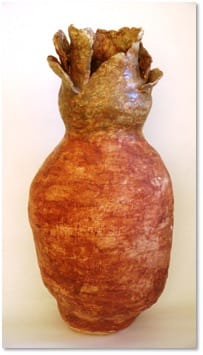 A tall rust-orange glazed jar crowned with a ragged collar of upturned petal shapes.